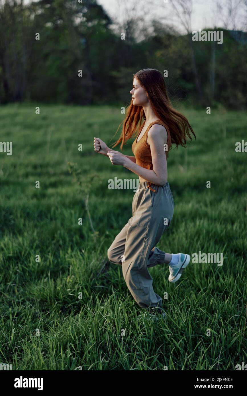 A young woman exercising outside and running in the park. in the evening on the green grass into the sunset Stock Photo