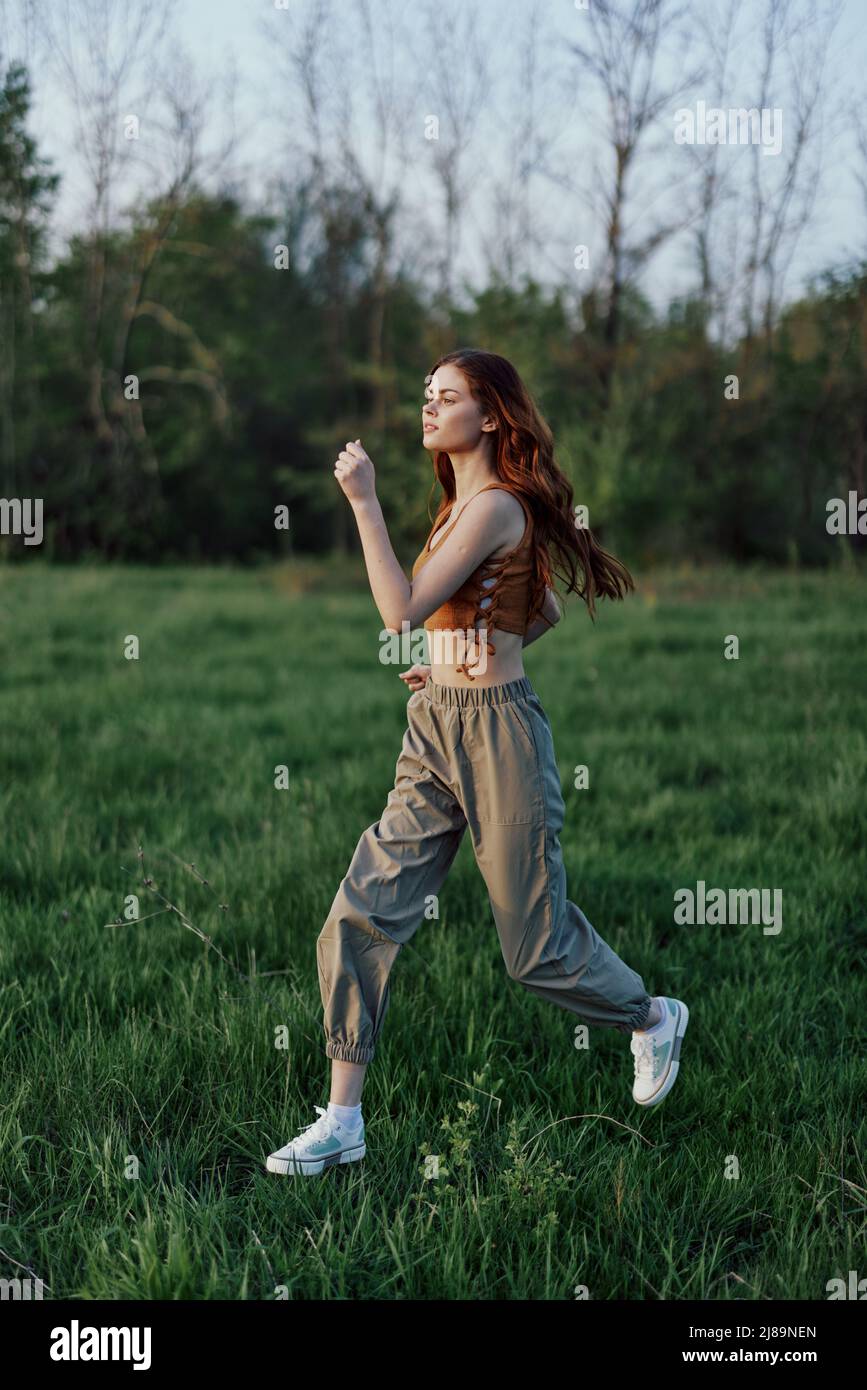 A young woman exercising outside and running in the park. in the evening on the green grass into the sunset Stock Photo