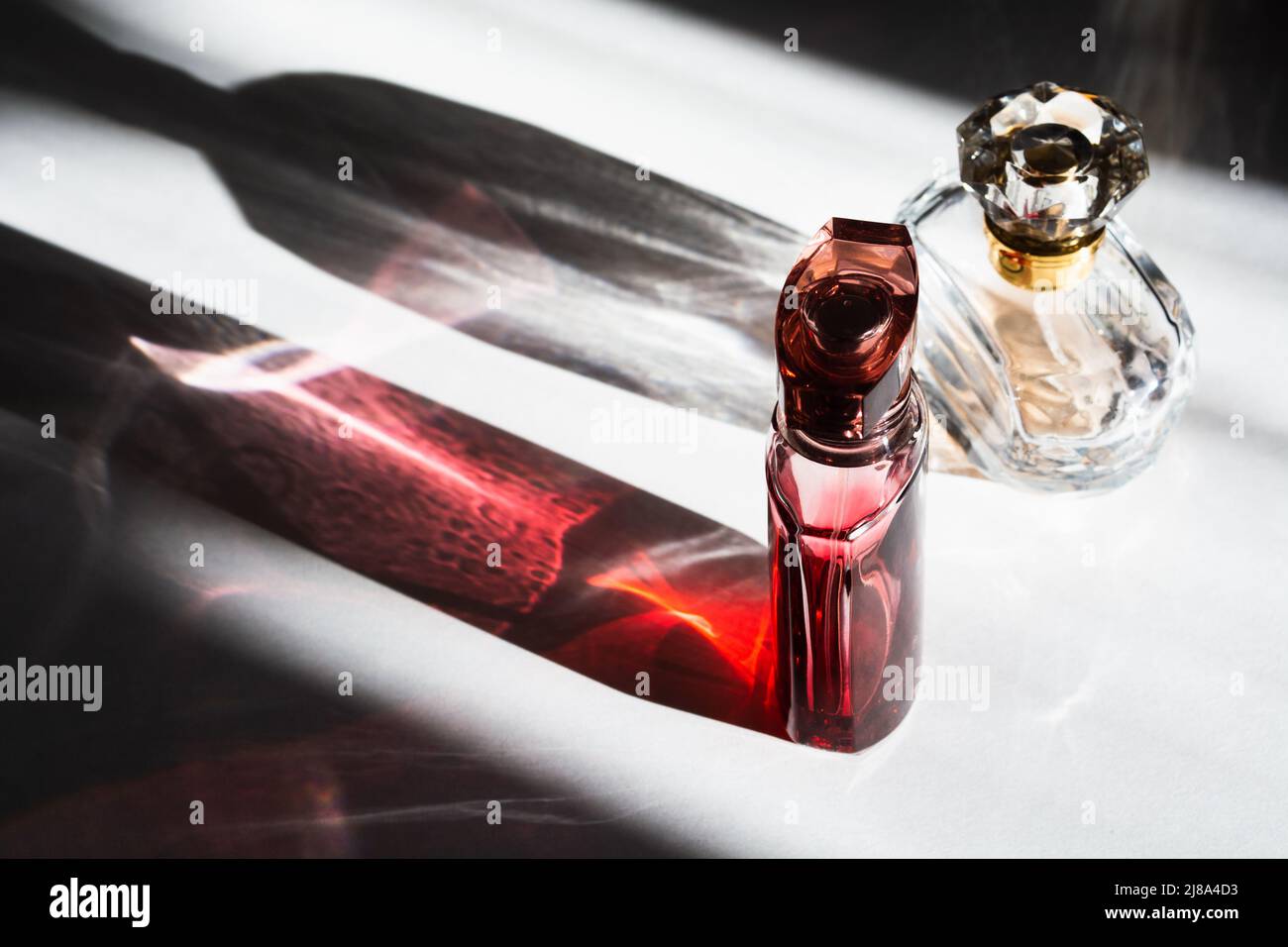 Two colorful transparent glass bottles of perfume with sunlight and shadows Stock Photo