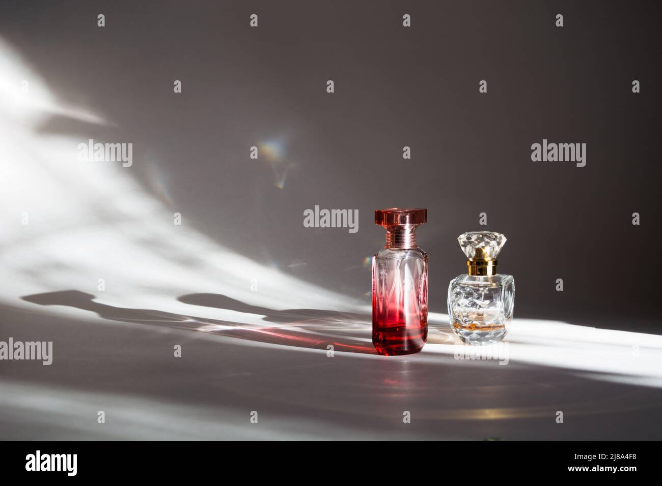 Two colorful transparent glass bottles of perfume with sunlight and shadows Stock Photo