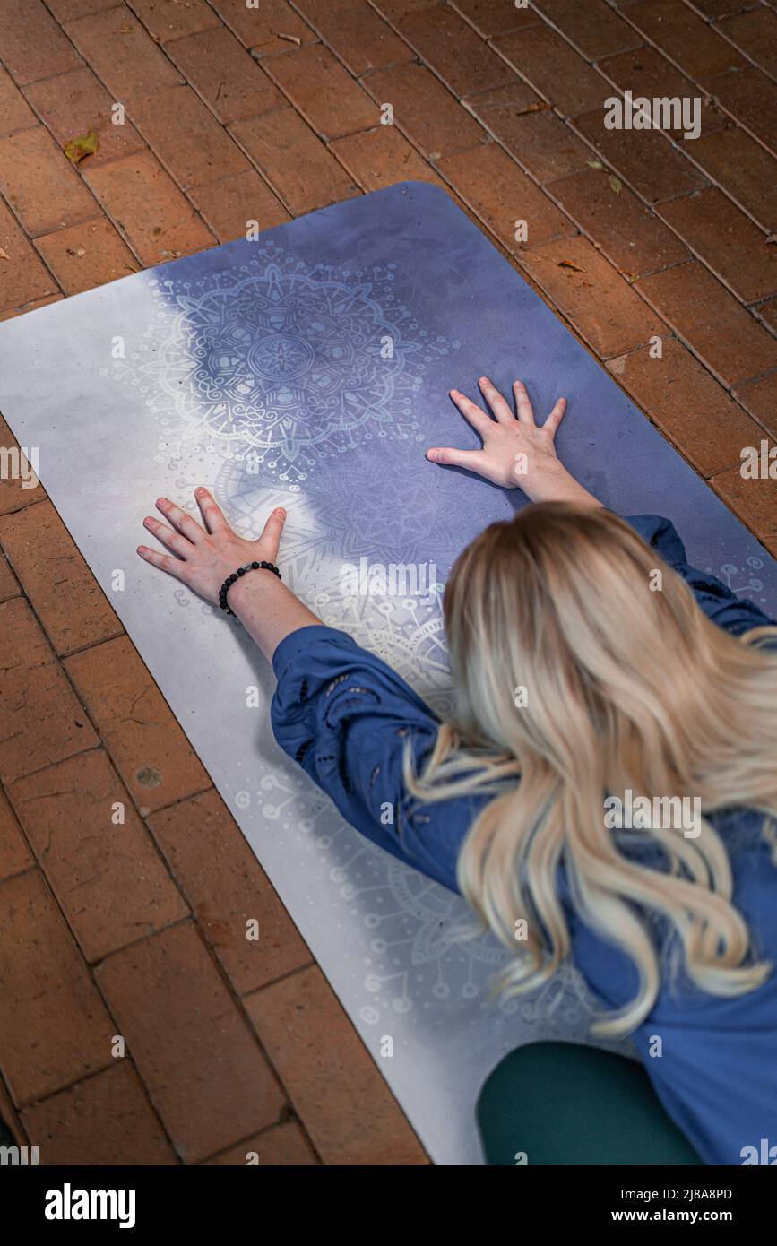 high angle shot from above of blonde caucasian spiritual lady in childs pose on her yoga mat focused on her long hair and widespread hands Stock Photo