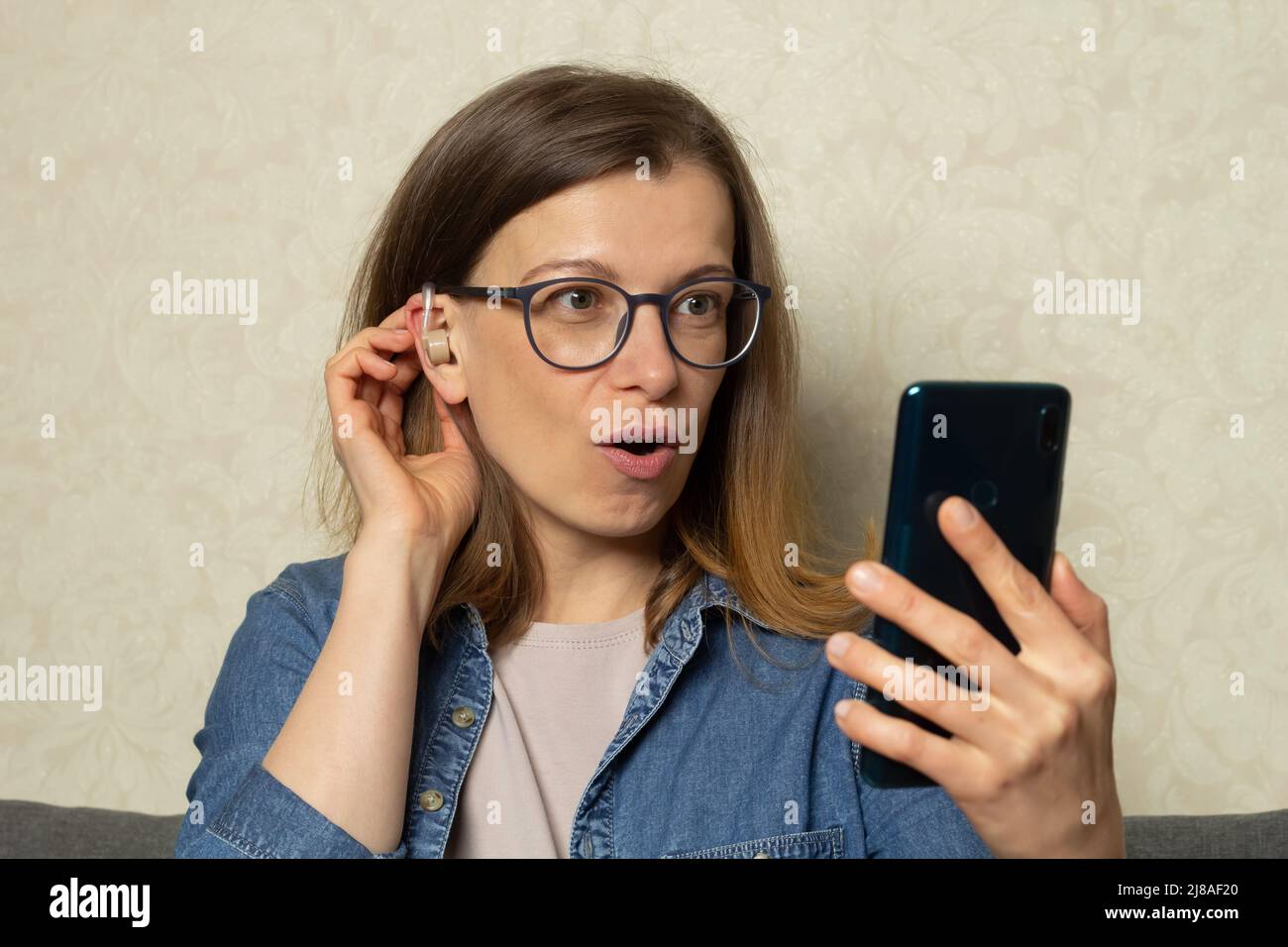 A woman is talking on the phone using a hearing aid on her ear to amplify the sound. Stock Photo