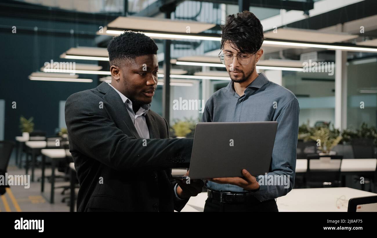 Two male business partners men Arabian man holding laptop showing presentation African businessman looking at computer screen colleagues working Stock Photo