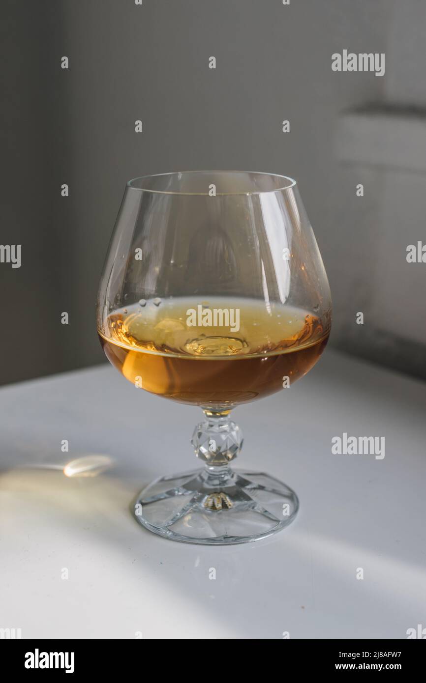 brandy snifter on white reflective table with white background by window Stock Photo