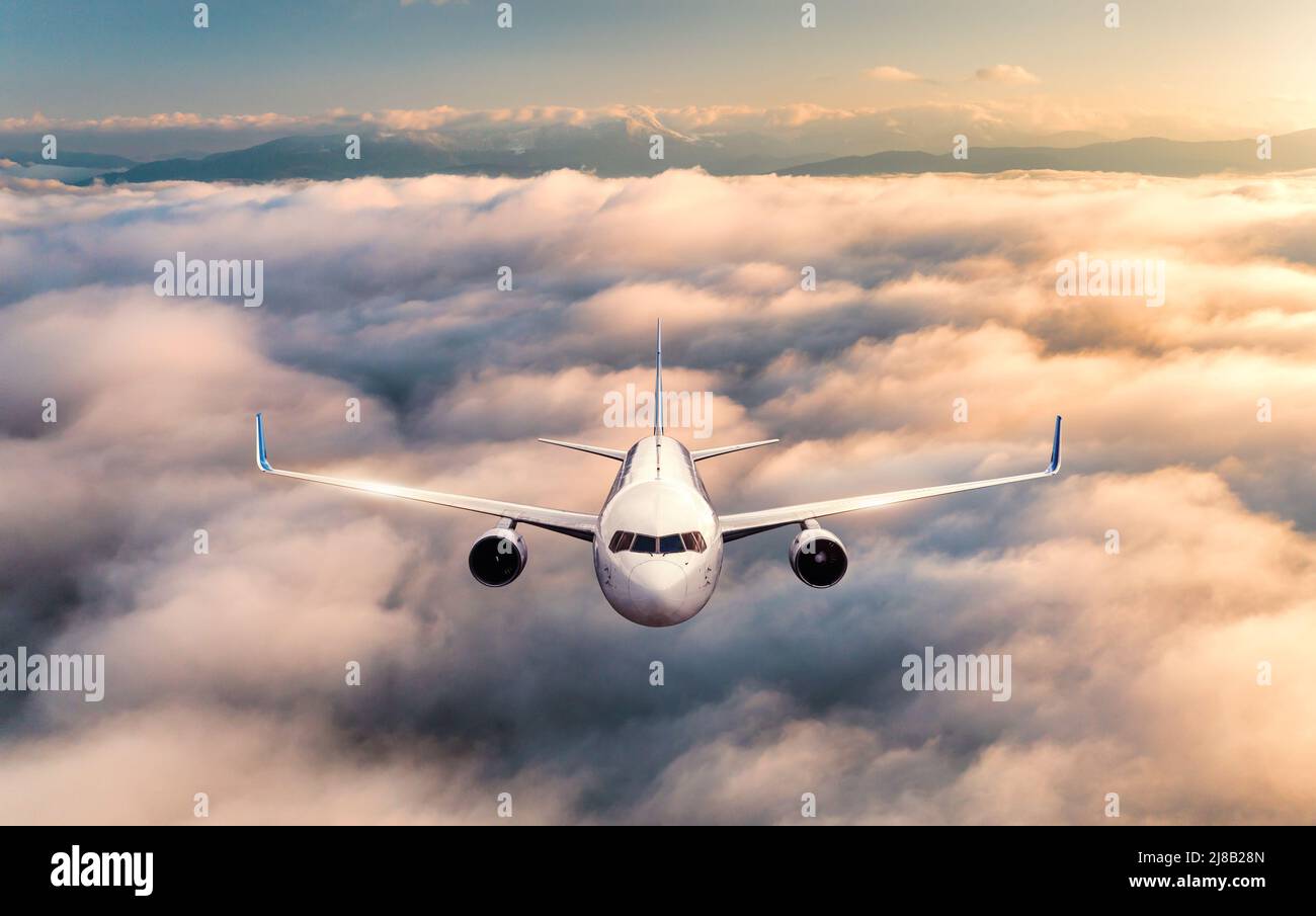 Airplane is flying above the clouds at sunrise in summer Stock Photo