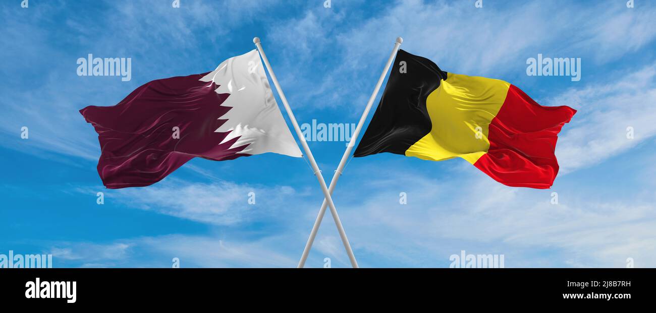 two crossed flags Qatar and Belgium waving in wind at cloudy sky ...