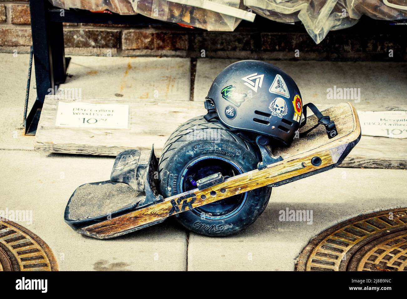 04 15 2022 Tulsa USA - Well used and slightly battered  one wheel electric skateboard with helmet covered with stickers parked on sidewalk outside gro Stock Photo
