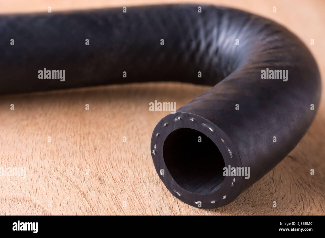 automotive hose, fluid carrying engine hose made of reinforced synthetic rubber on a wooden table top, closeup macro with copy space Stock Photo