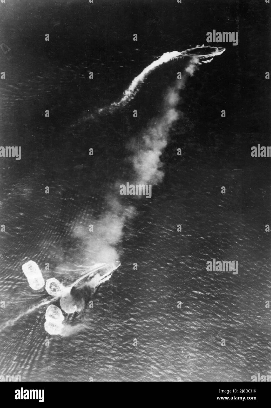 Loss of HMS Prince of Wales and HMS Repulse, 10 December 1941: Photograph taken from a Japanese aircraft during the initial high-level bombing attack. The battlecruiser Repulse, near the bottom of the view, has just been hit by one bomb and near-missed by several more. The battleship Prince of Wales is near the top of the image, generating a considerable amount of smoke. Stock Photo