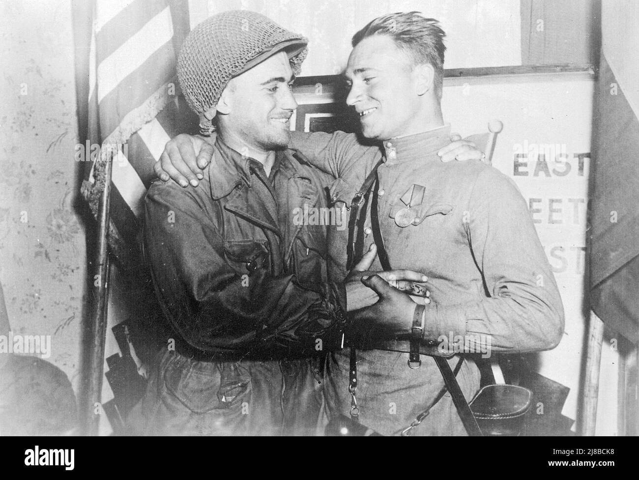 An American soldier (2nd Lt. William Robertson, US Army) and a Red Army soldier (Lt. Alexander Sylvashko, Red Army) meeting during the allied invasion of Germany. The photo is a staged propaganda piece, with the nations flags and the East Meets West sign behind. Stock Photo