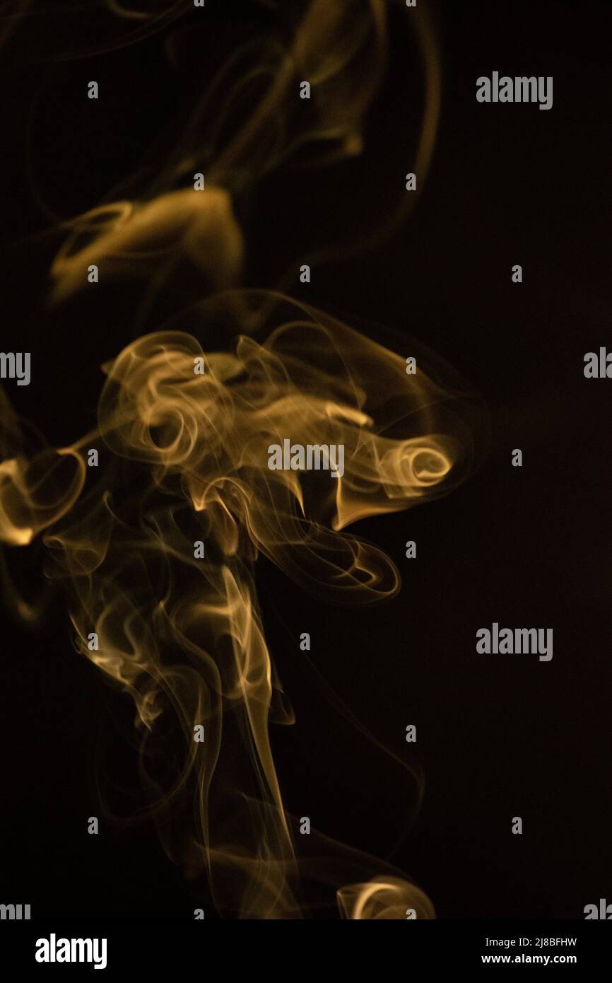 Golden yellow swirling, ascending smoke pattern on a black background, photo could be used as a background, smoke texture, abstract, or general stock Stock Photo