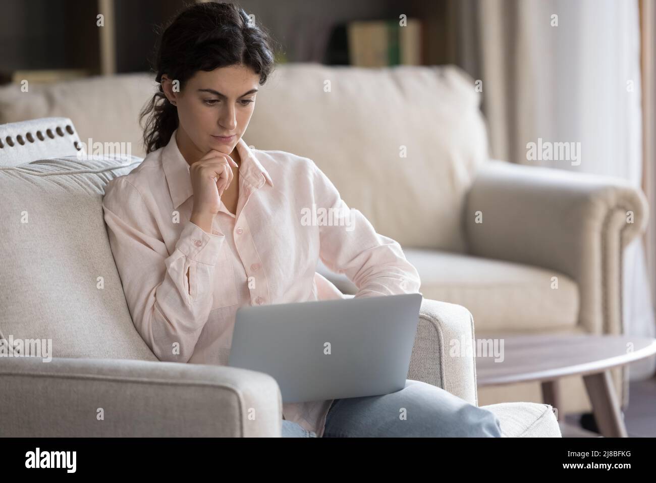 Thoughtful woman spend leisure using laptop sit on couch indoor Stock Photo
