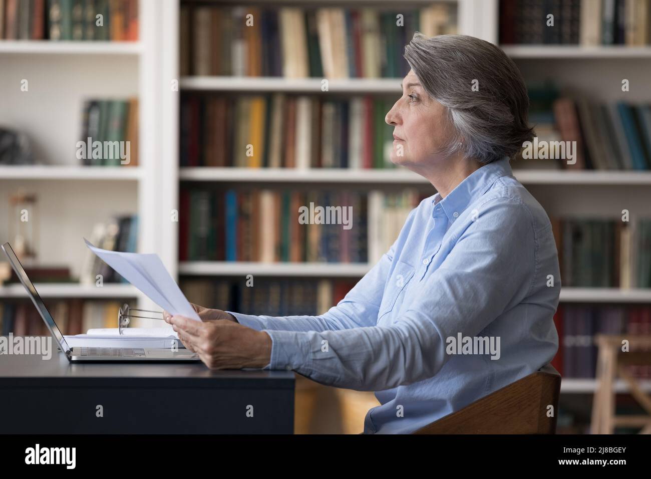 Serious concentrated older business woman analyzing paper documents ...