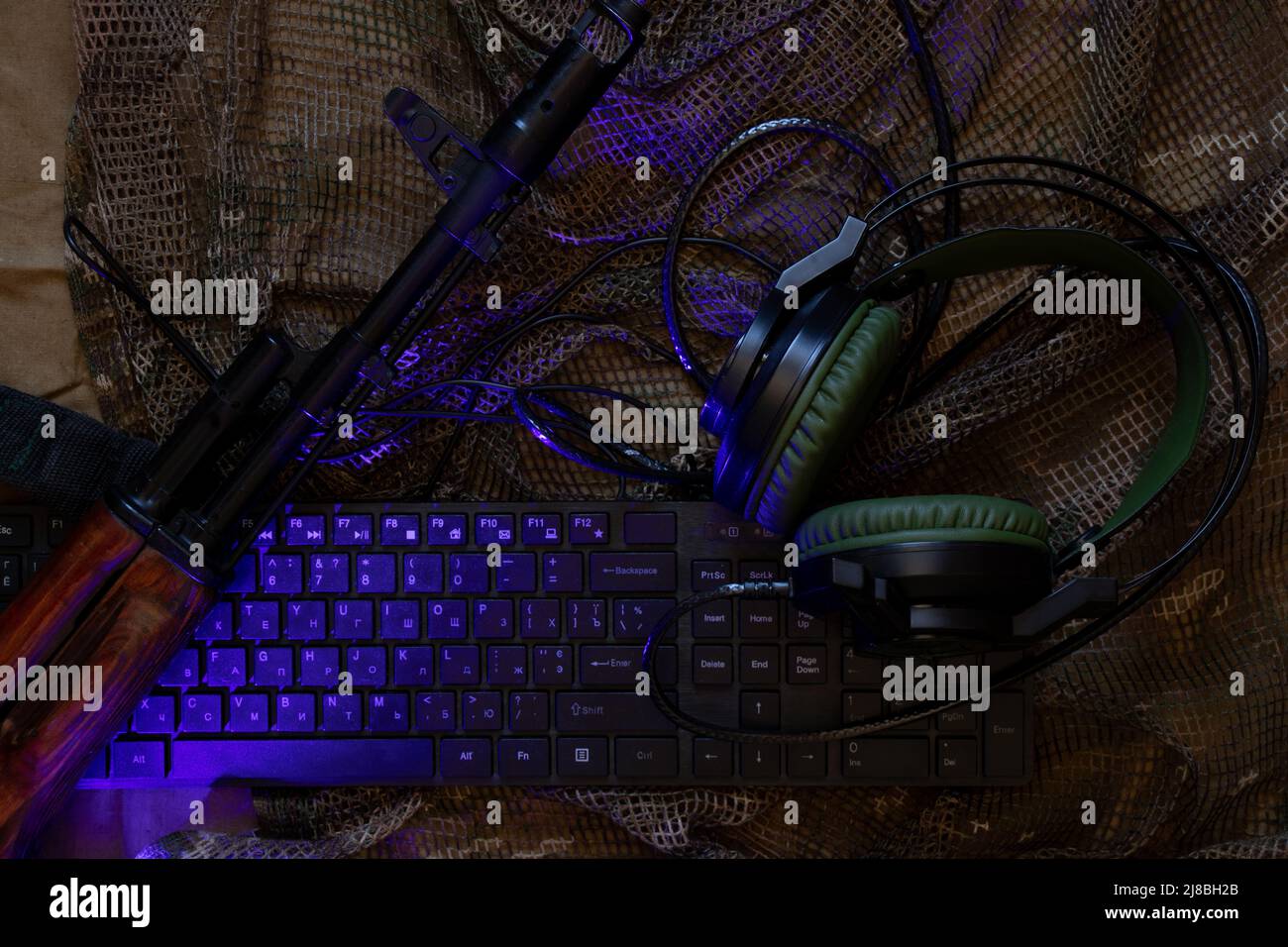 The keyboard of a military combat machine and headphones lie on a camouflage camouflage net, cyber police, online attack, technology Stock Photo