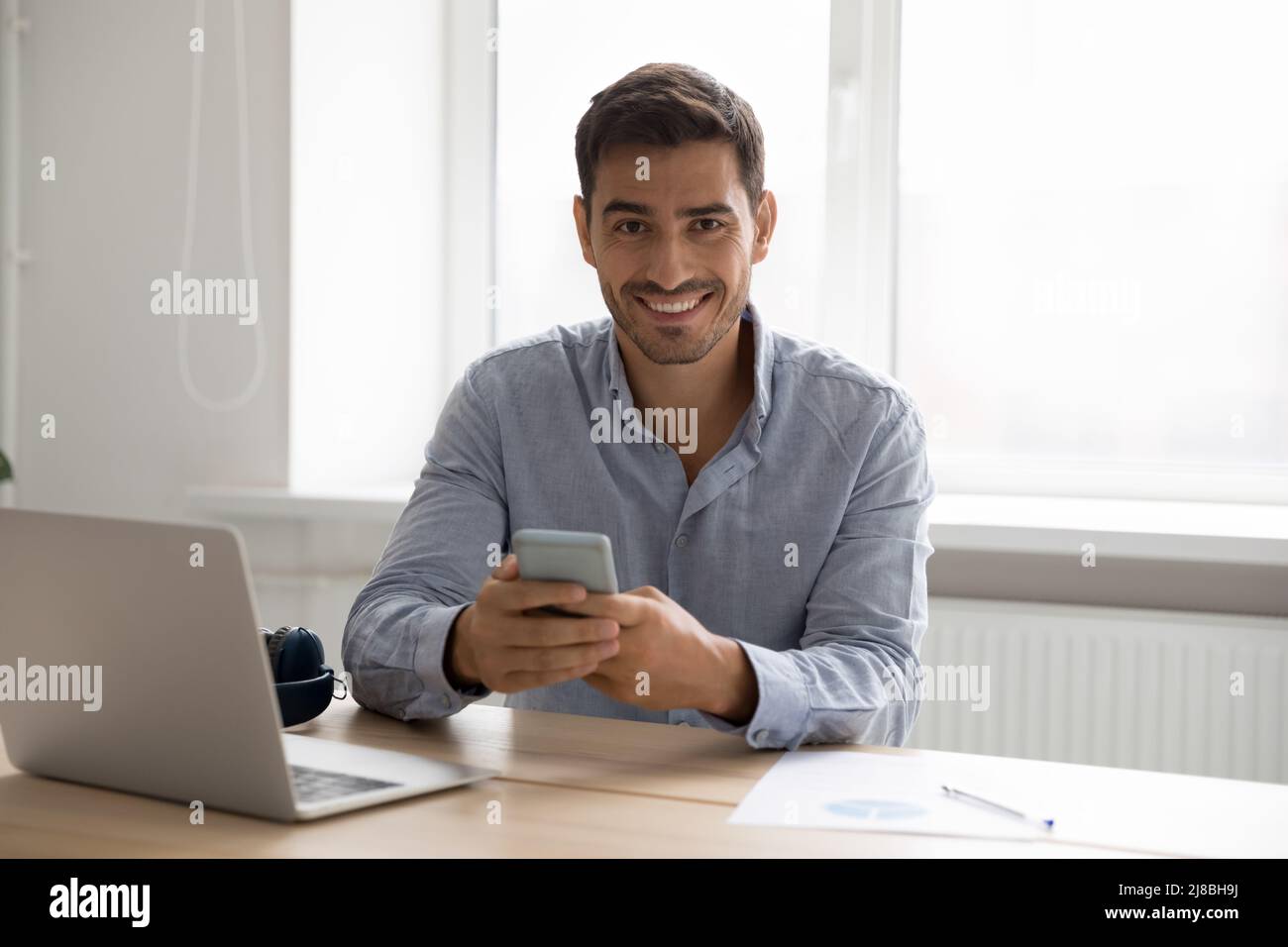Happy gadgets user man using smartphone, laptop at home workplace Stock Photo