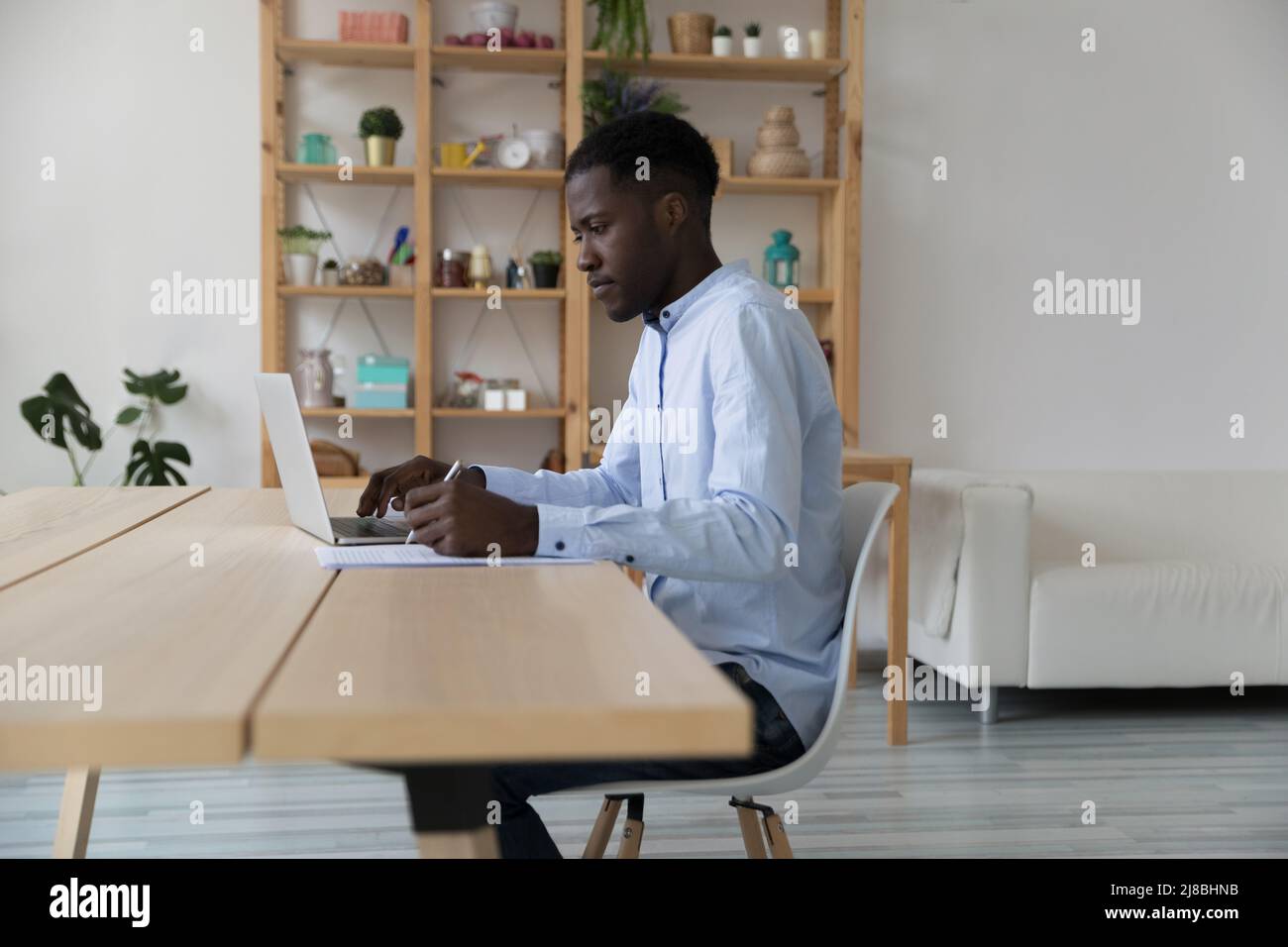 Serious busy African freelance employee writing in paper document Stock Photo