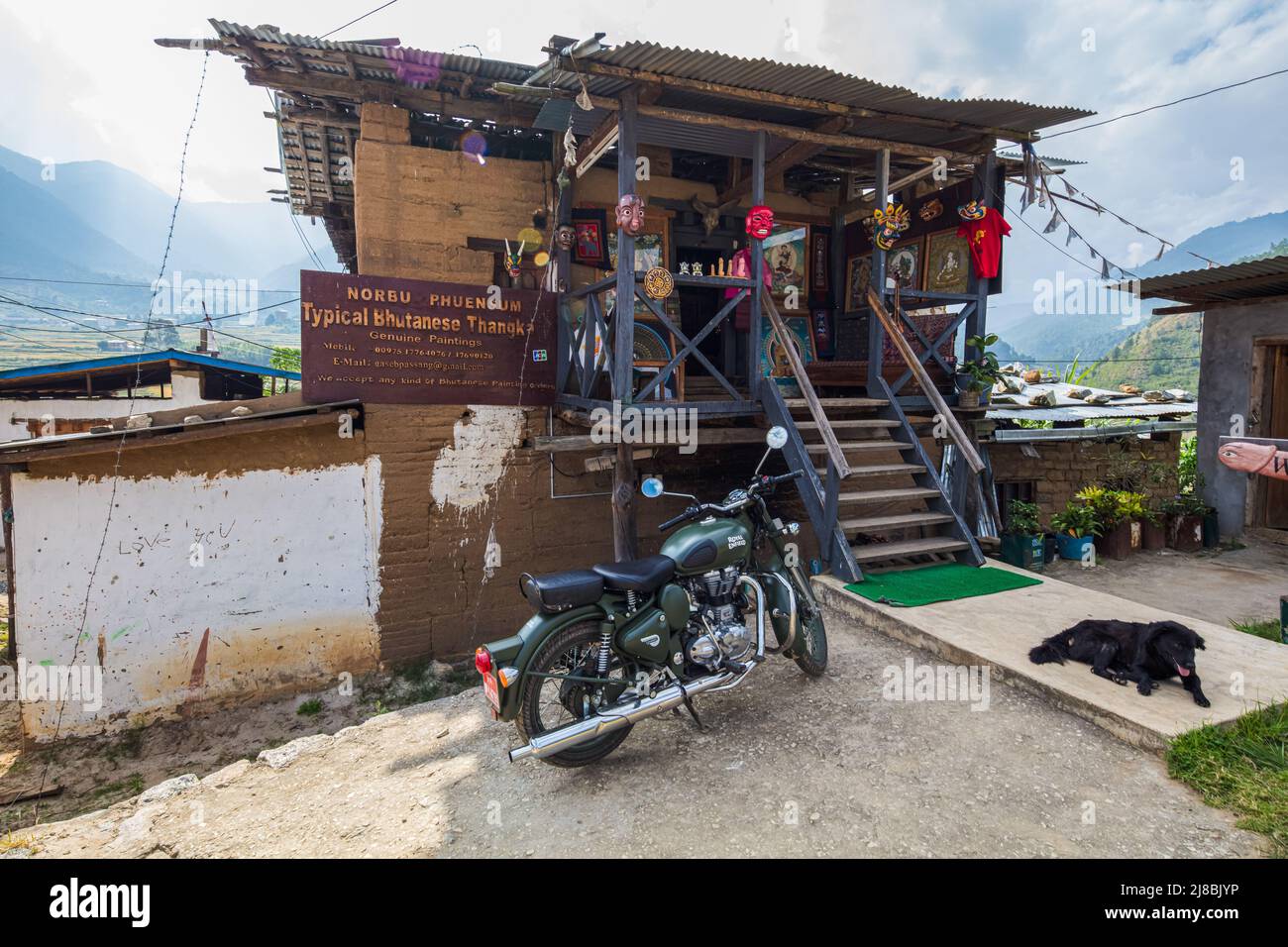 Paro, Bhutan - October 24, 2021: Art shop in an old rather dilapidated traditional house. Indian Royal Enfield motorcycle and a black dog is in front Stock Photo