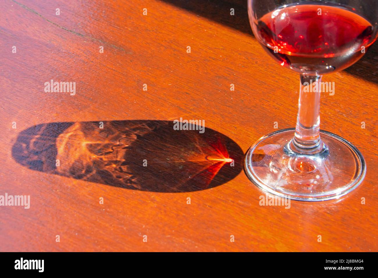 A half full glass with red wine and its reflections building wonderful shapes Stock Photo