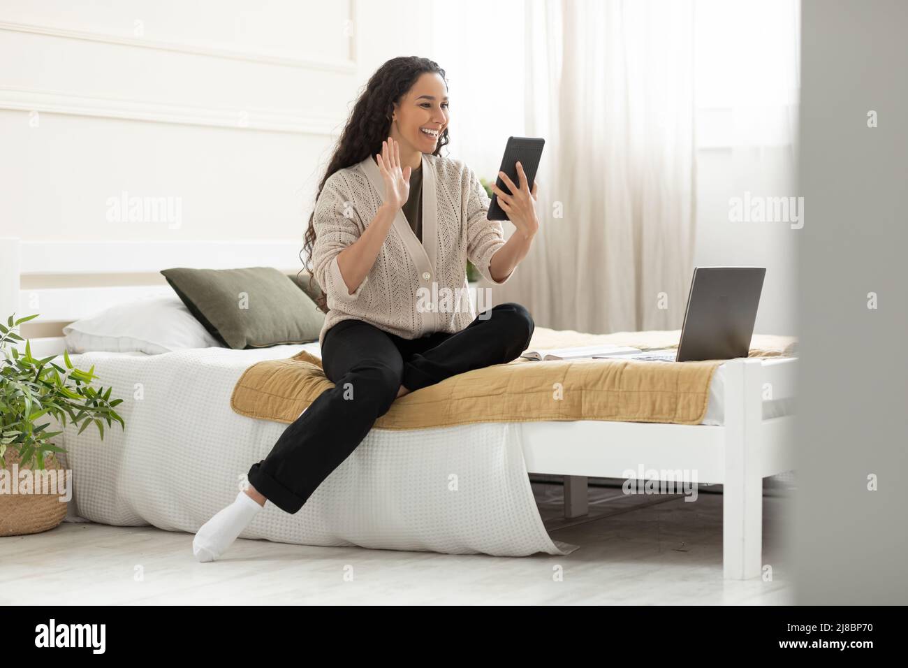 Smiling young woman waving hand using digital tablet Stock Photo