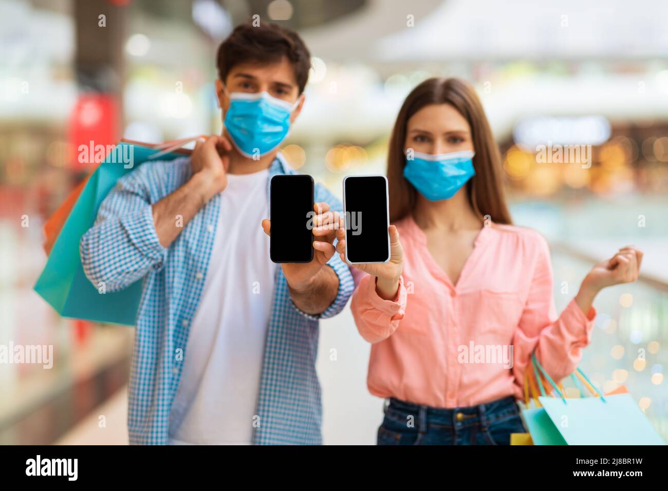 Couple On Shopping Showing Smartphones Wearing Masks In Modern Mall