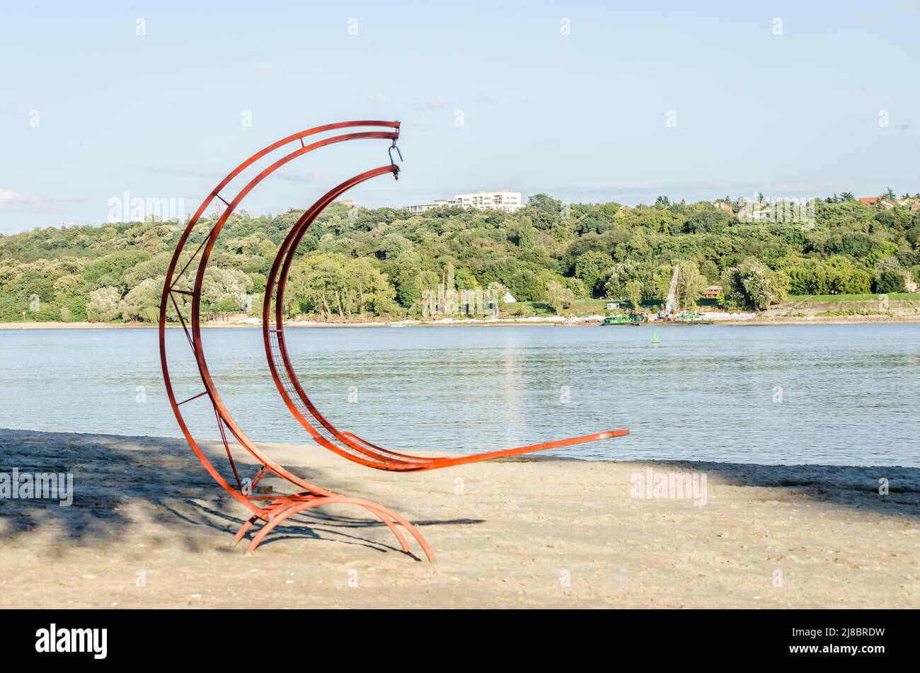 Red metal deck chair on the beach of the Danube river. Stock Photo