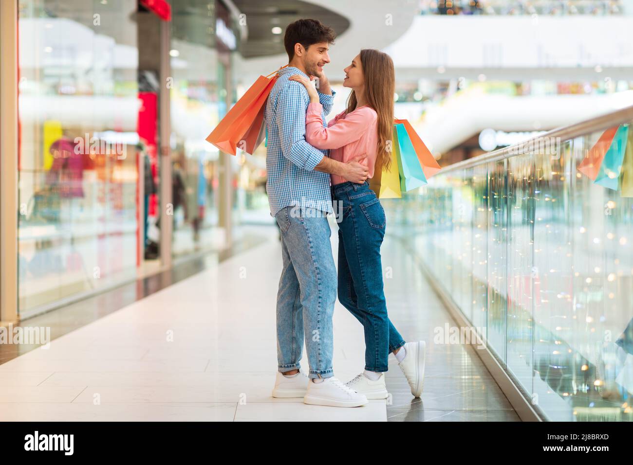 Couple On Shopping Hugging Holding Shopper Bags Standing In Hypermarket Stock Photo