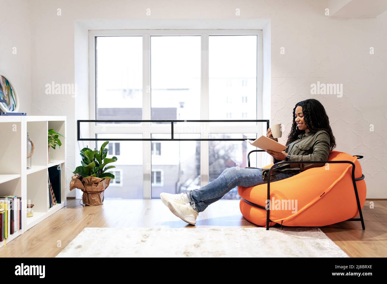 Smiling black woman reading book and drinking coffee Stock Photo - Alamy