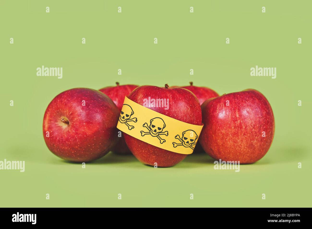 Apples with poison skull symbol sticker on green background. Concept of pesticide residues in agricultural food Stock Photo