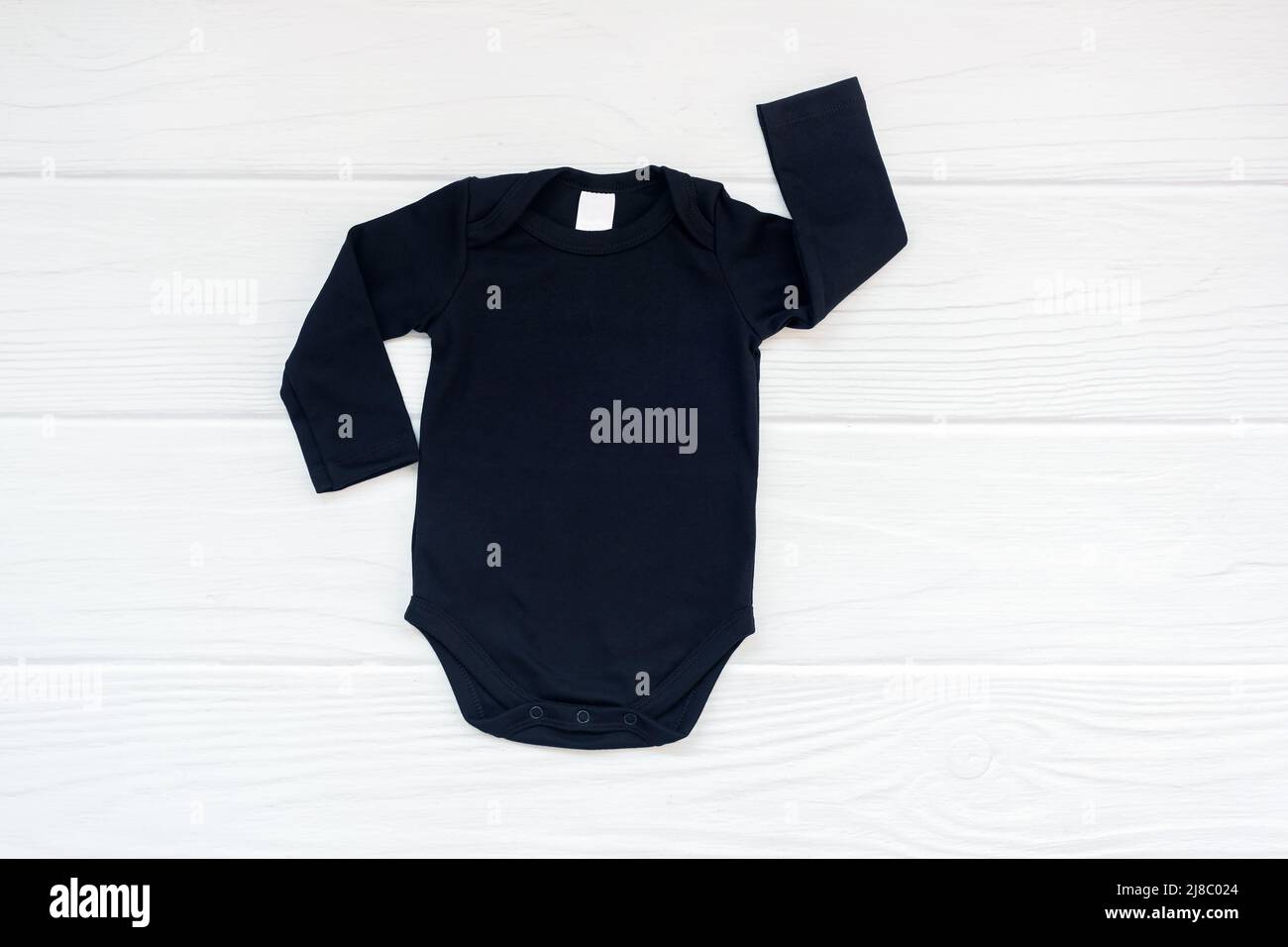Simple black baby bodysuit long sleeve flatlay mockup on white wood background. Stock Photo
