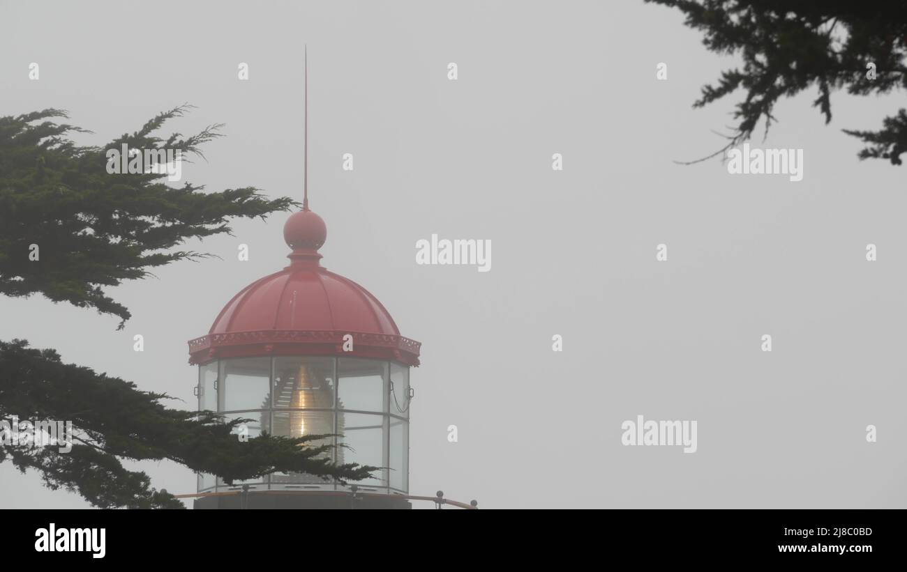 Point Pinos old historic lighthouse fresnel lens glowing, foggy rainy bad weather. Illuminated retro vintage light house, beacon tower, misty forest. California coast USA. Seamless looped cinemagraph. Stock Photo