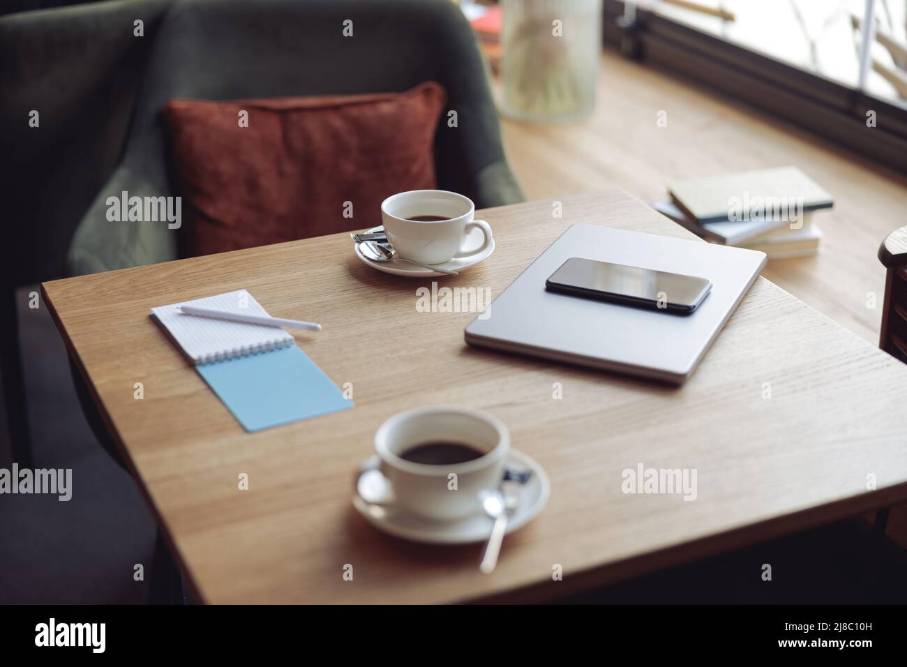 Wooden table with two white cups of coffee and business stuff. Laptop, notebook and phone. Stock Photo