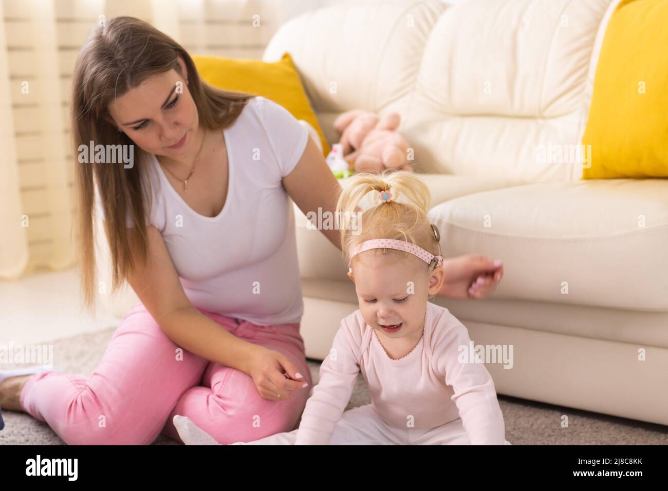Happy child girl with cochlear implant having fun with her mother - hearing aid for deaf and innovative health technology concept Stock Photo