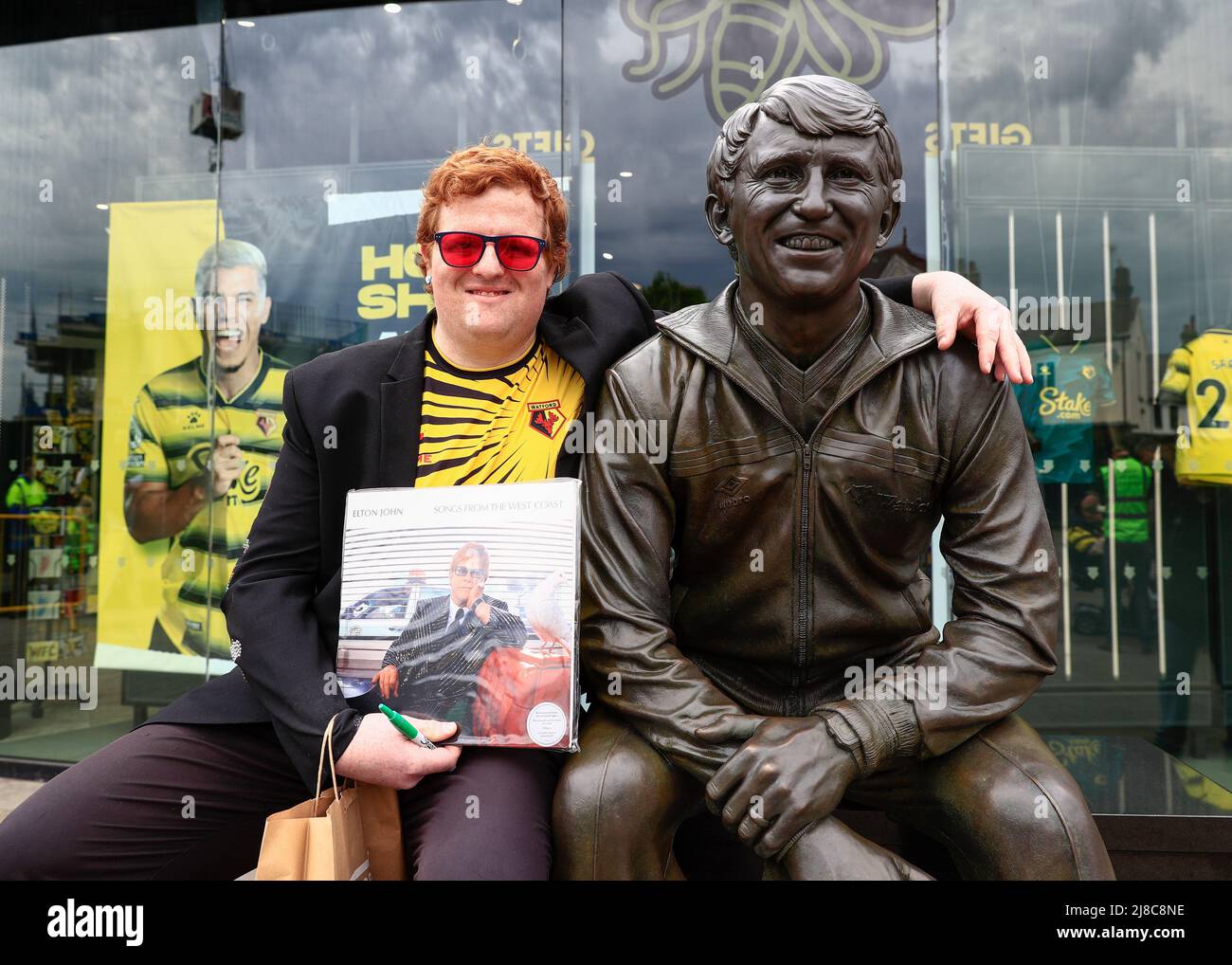 Watford, Herts, UK. 15th May 2022 ;   Vicarage Road, Watford, Herts,  England;  Premier League football, Watford versus Leicester City; An Elton John Watford fan poses with the Graham Taylor statute outside Vicarage Road Stadium Credit: Action Plus Sports Images/Alamy Live News Credit: Action Plus Sports Images/Alamy Live News Stock Photo