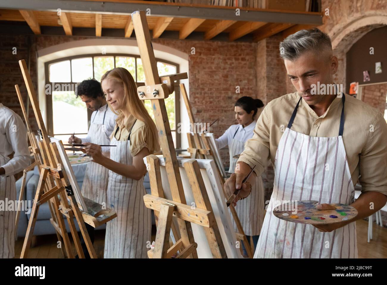 Handsome millennial painter man painting during group art-class Stock Photo