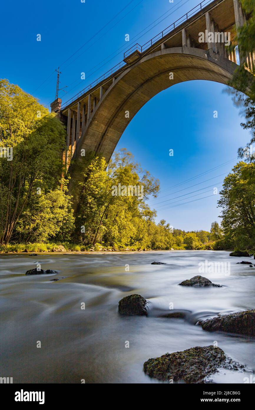 High long railway bridge over small river full of big stones at sunny day Stock Photo