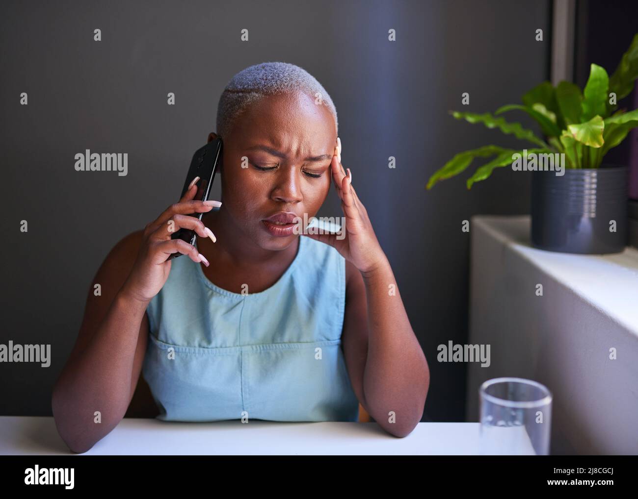 A young Black businesswoman holds her head while on hold on a stressful call Stock Photo
