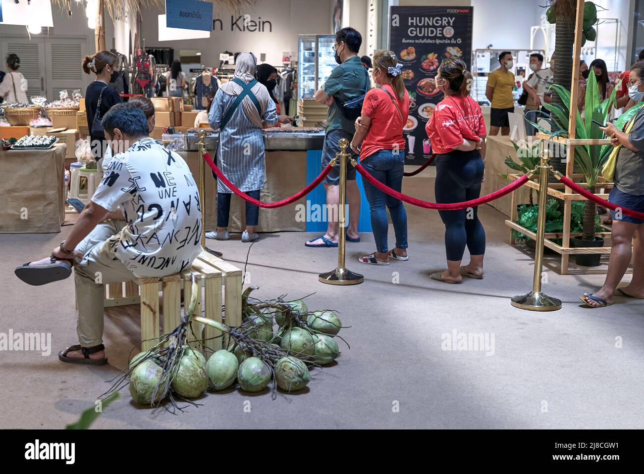 People queuing inside in a roped off cordoned area for a coconut food delicacy in a Thailand shopping mall. Southeast Asia Stock Photo
