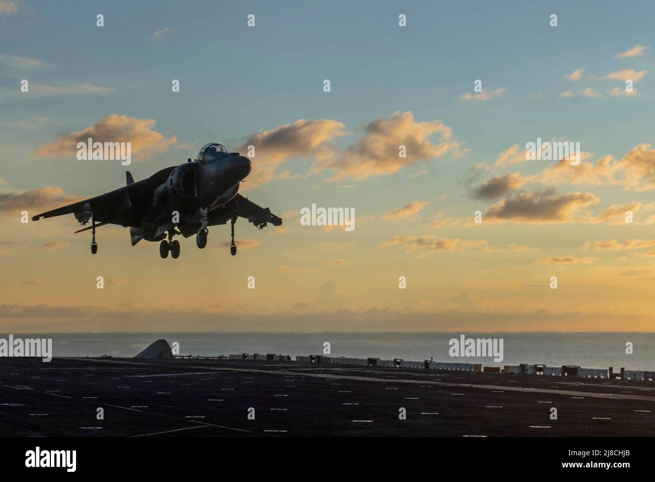 A U.S. Marine Corps AV-8B Harrier II, attached to the Marine Medium Tiltrotor Squadron 163, performs a vertical landing on the flight deck of the Wasp-class amphibious assault ship USS Boxer at sunset, October 3, 2019 on the South China Sea. Stock Photo