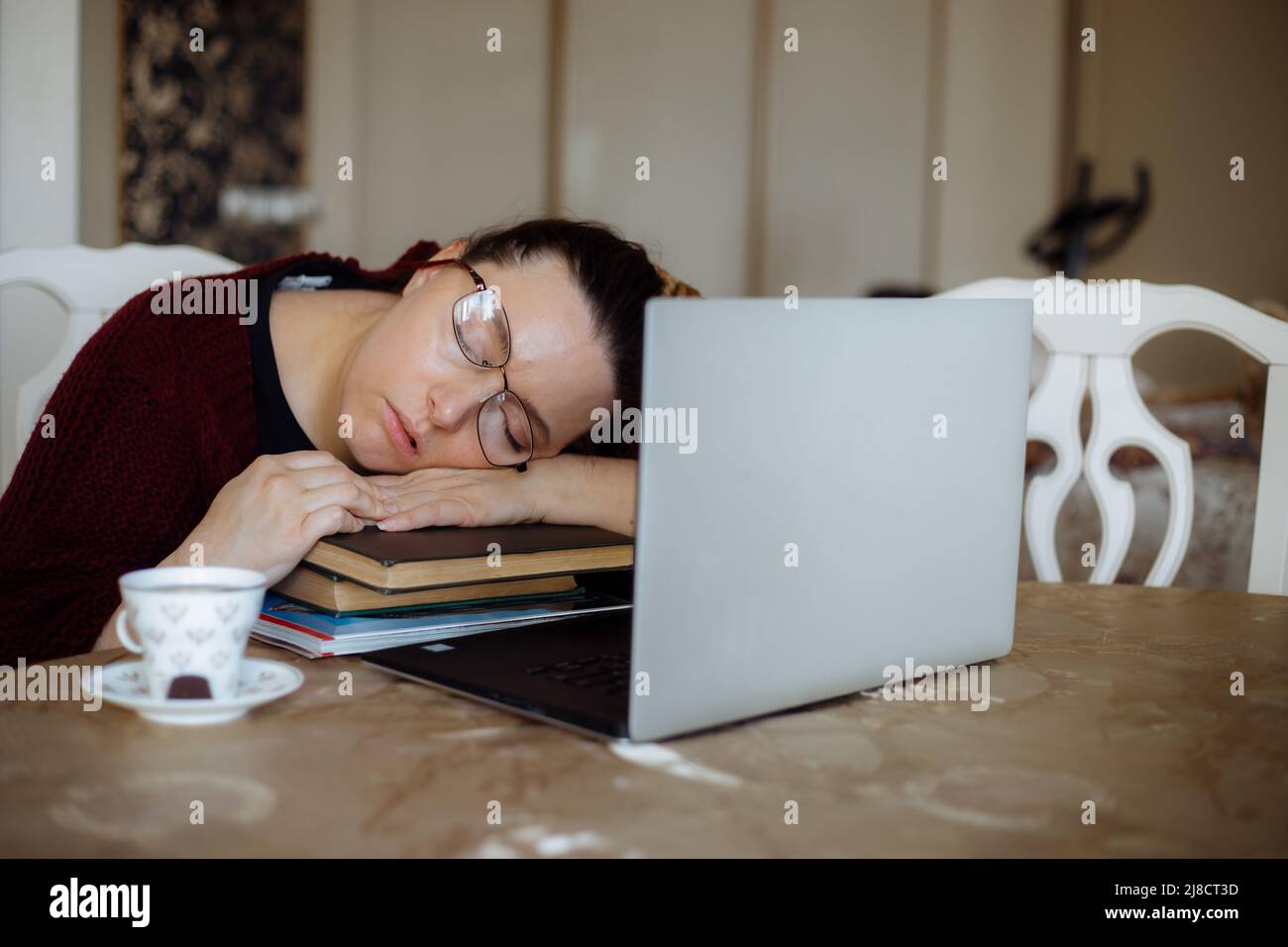 Tired young woman in glasses sleeping on books near laptop at desk in home room. Tiredness from monotonous study and rest at workplace from computer Stock Photo