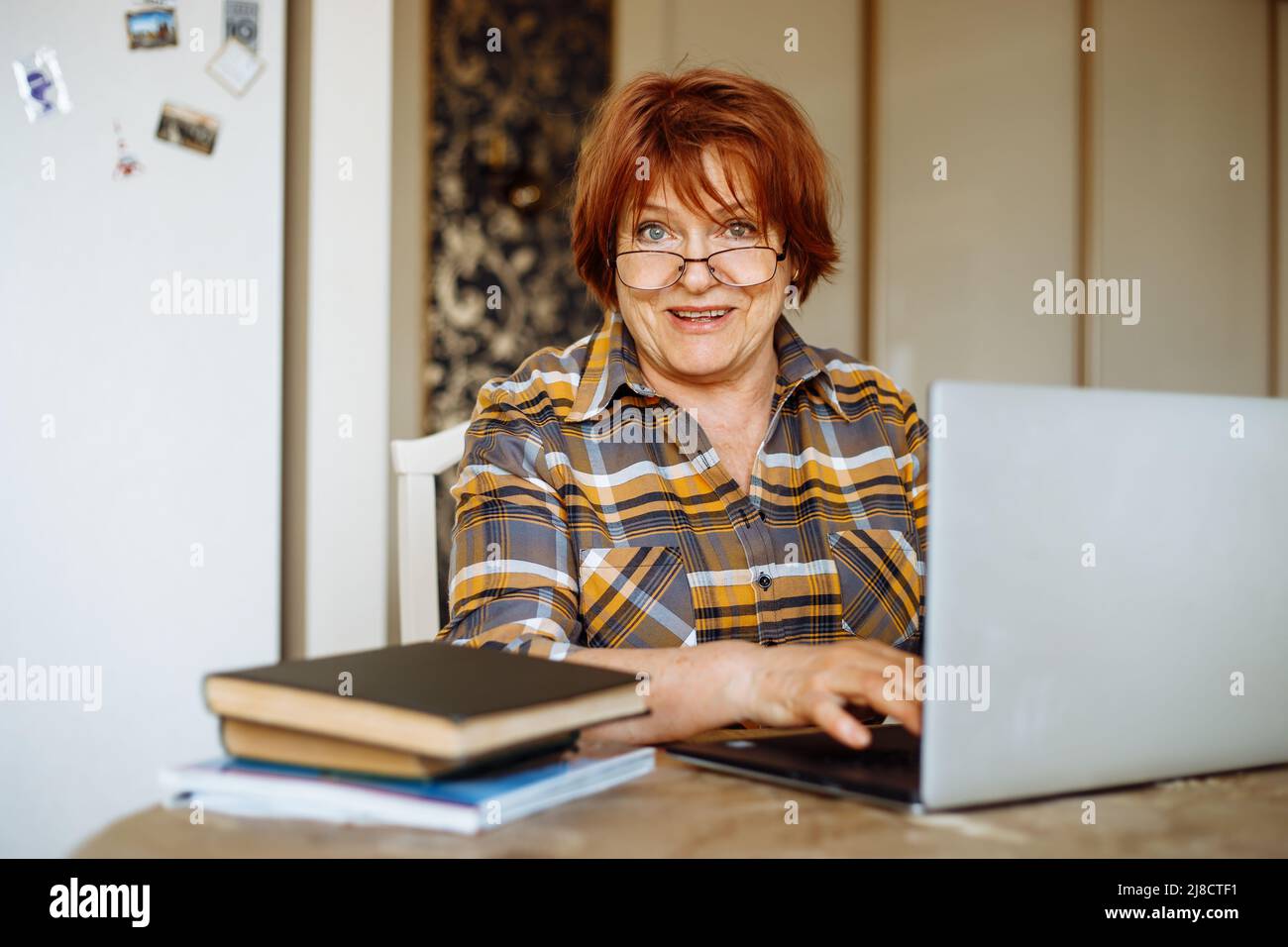 Happy mature lady typing on laptop sitting at desk in room and practicing computer skills. Advanced pensioner using and learning modern technology Stock Photo