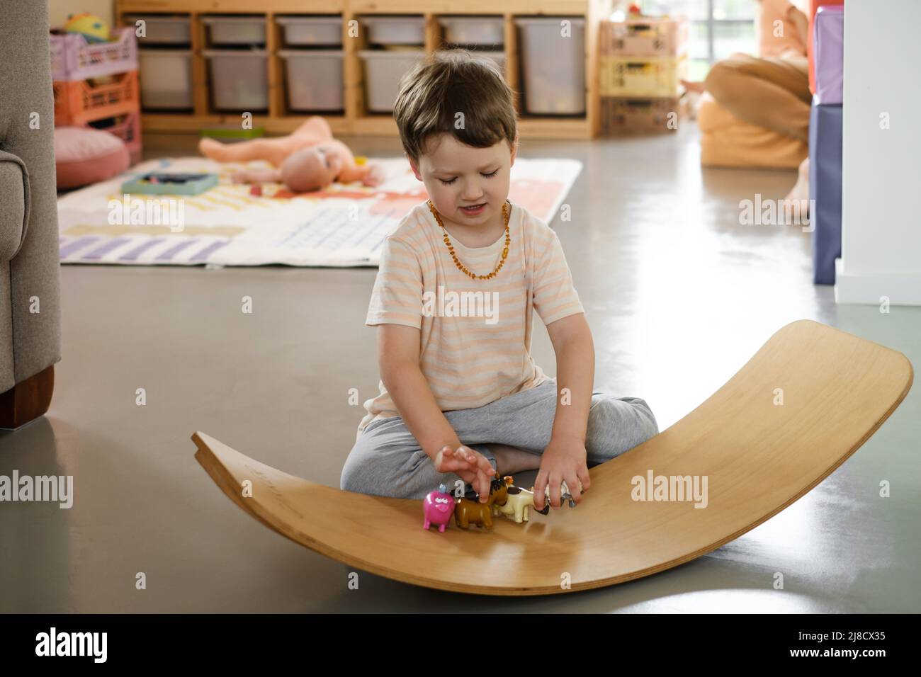 Child playing on balance Board for Toddlers in kids room. Curvy Rocker Board used for motor physical development at home. Boy playing, get fit Stock Photo