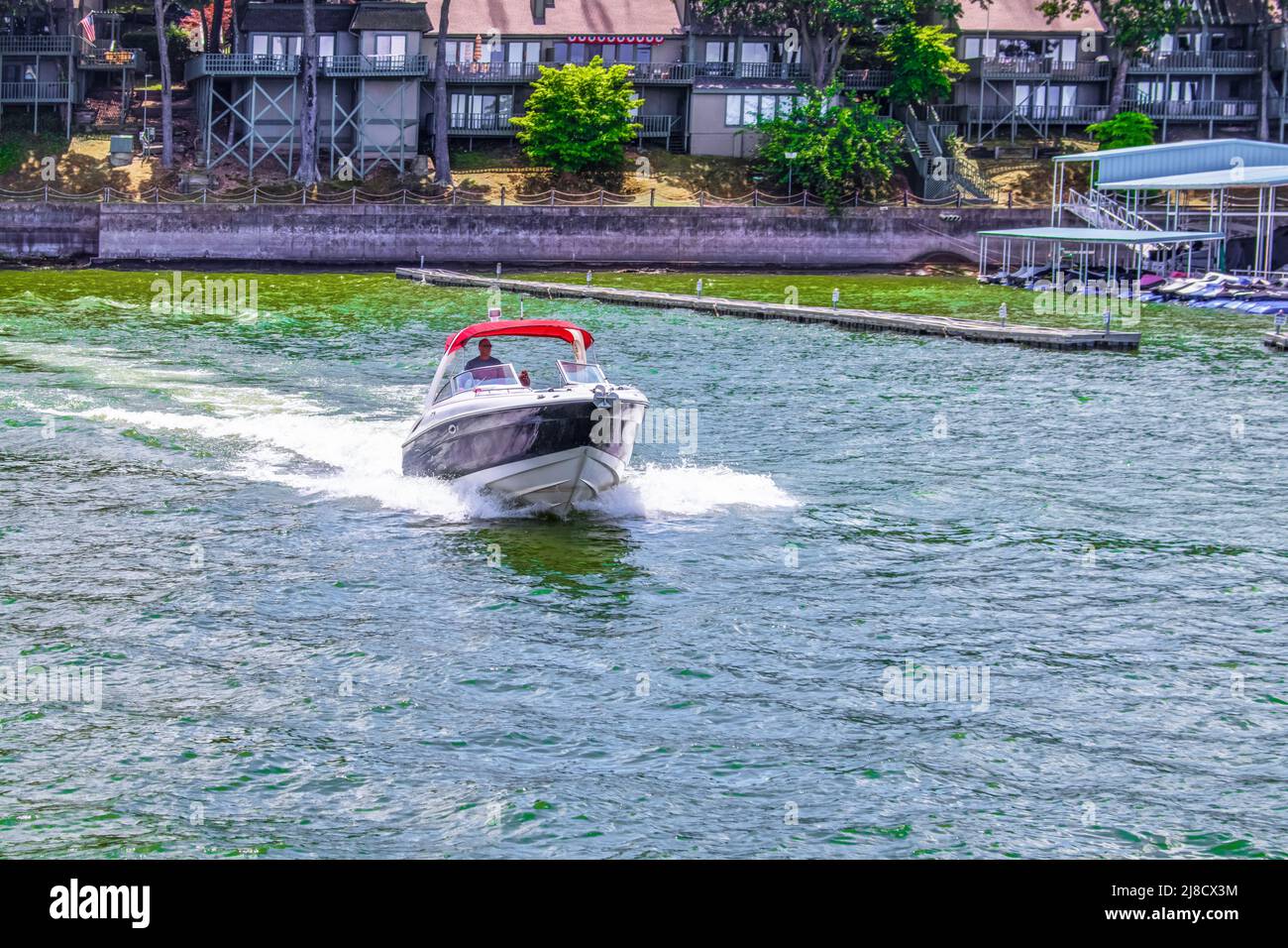 Speedboat speeds across a lake with condos and docks and a long pier on and near the shore on a summer day Stock Photo
