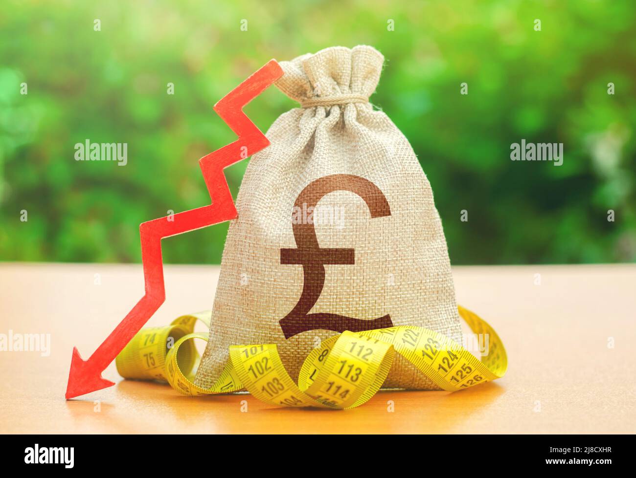 British pound sterling money bag with down arrow and measure tape. Falling wages and welfare. Reduced wages, cuts in social benefits. Cutting costs, s Stock Photo