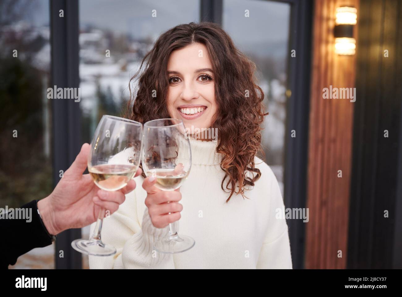 Happy couple toasting with wine enjoying alcoholic drink and celebrating together outdoors. Cheerful woman looking to the camera and smiling while clinking wine glasses. Celebration concept. Stock Photo
