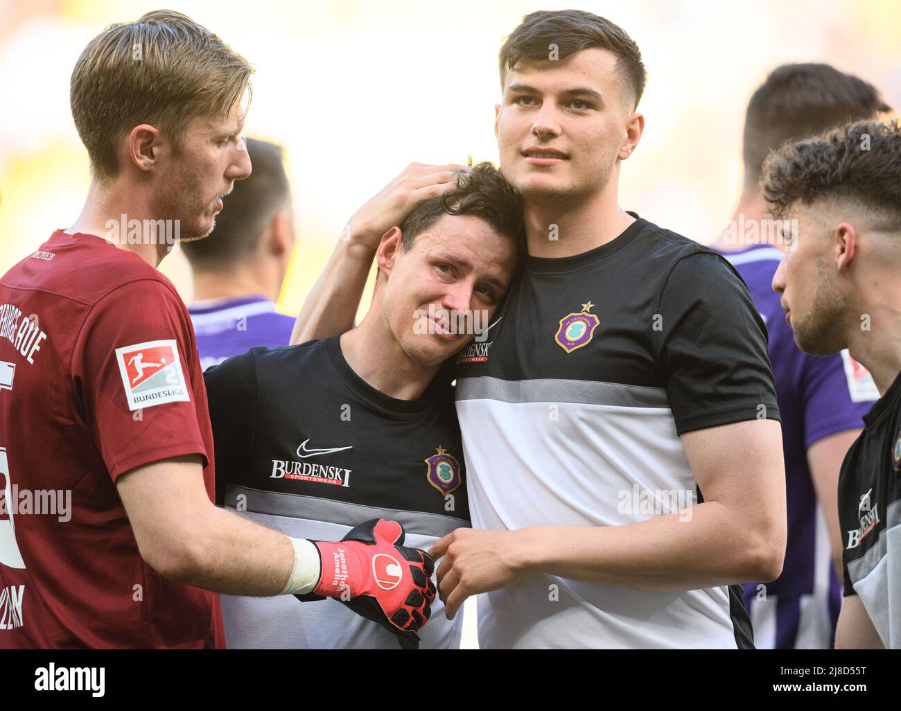 15 May 2022, Saxony, Dresden: Soccer: 2nd Bundesliga, SG Dynamo Dresden - FC Erzgebirge Aue, Matchday 34, Rudolf Harbig Stadium. Aue's Clemens Fandrich (M) cries after the win and is comforted by goalkeeper Philipp Klewin (l) and Ramzi Ferjani. Photo: Robert Michael/dpa - IMPORTANT NOTE: In accordance with the requirements of the DFL Deutsche Fußball Liga and the DFB Deutscher Fußball-Bund, it is prohibited to use or have used photographs taken in the stadium and/or of the match in the form of sequence pictures and/or video-like photo series. Stock Photo