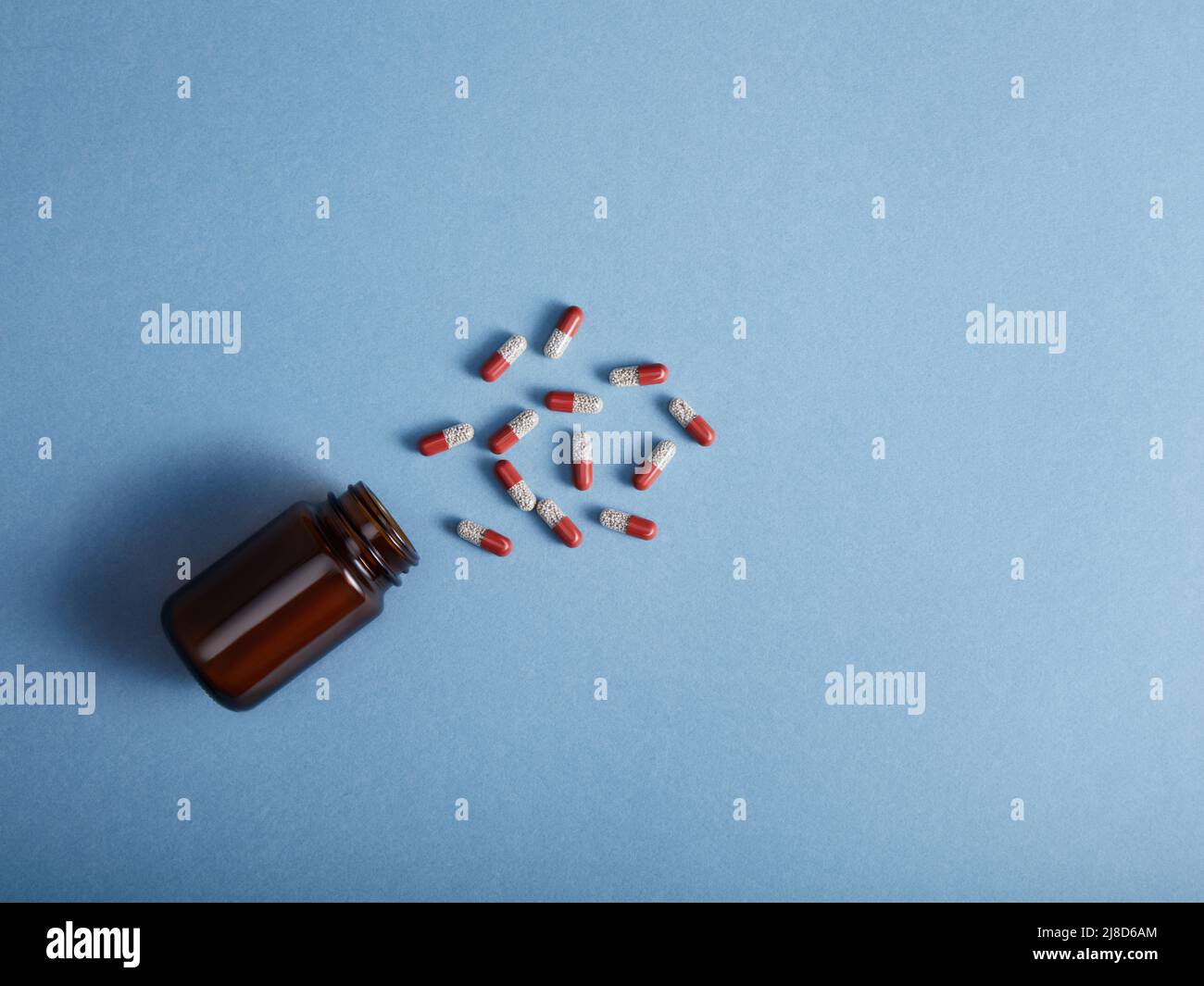 Pills spilling from a amber bottle, on blue paper background Stock Photo