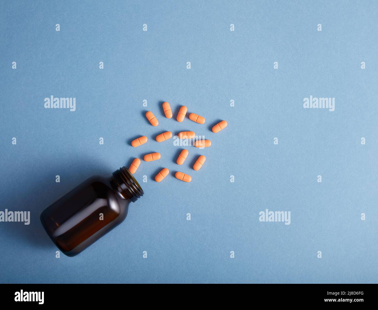 Pills spilling from a amber bottle, on blue paper background Stock Photo