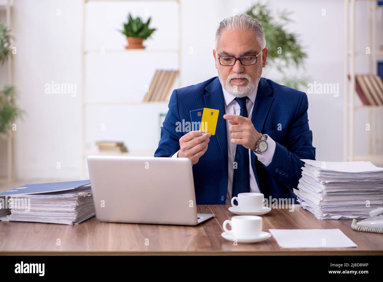Old businessman employee holding credit card at workplace Stock Photo