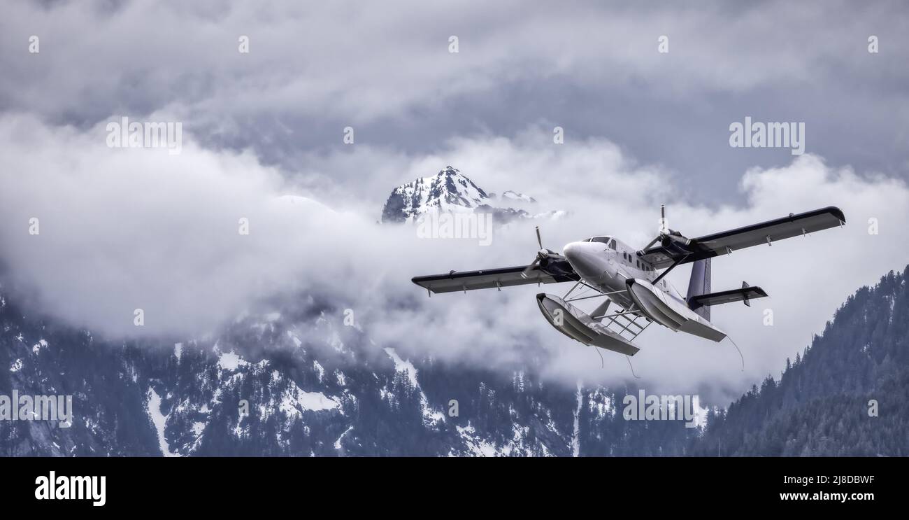 Seaplane Flying over the Rocky Mountains covered in snow and clouds. Stock Photo