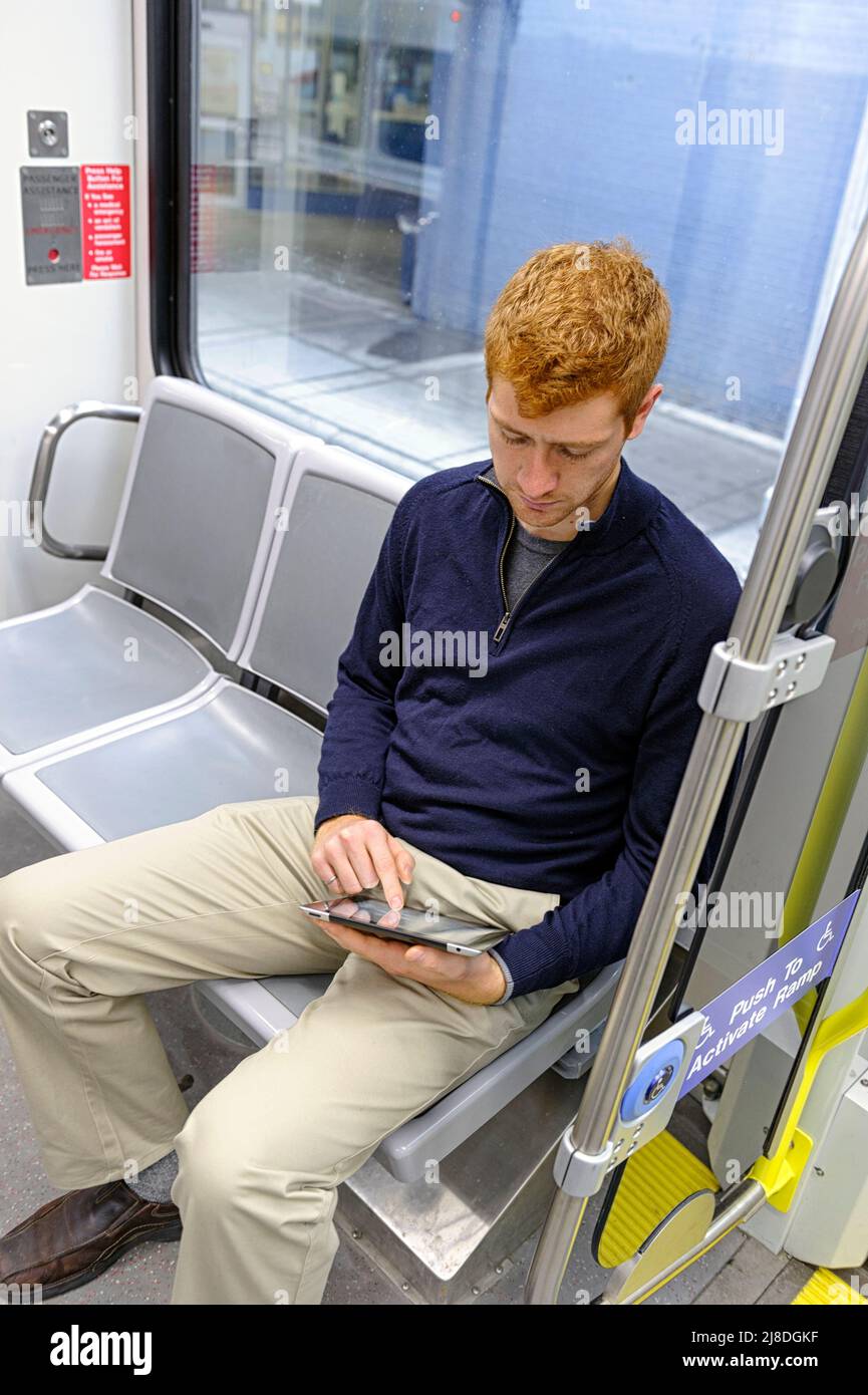 A young man with red hair using a electronic communication  device while using public transit Stock Photo